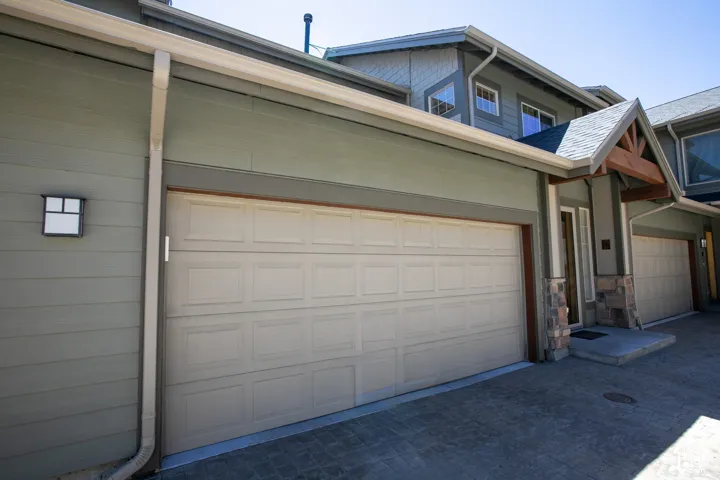 Multi-level exterior featuring horizontal lap siding, stone veneer accents, timber-frame entryway detail, and multi-car garage with paneled doors