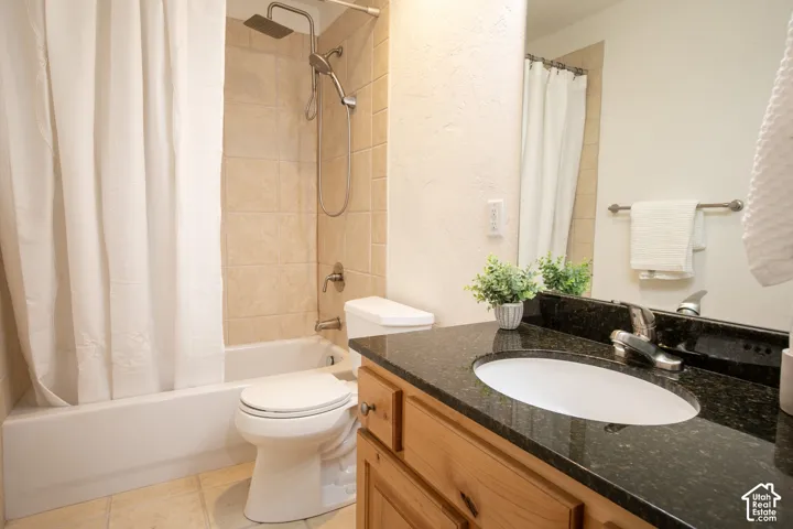 Bathroom featuring a vanity with dark stone countertop, undermount sink, shower with tile surround, and adjustable handheld shower head
