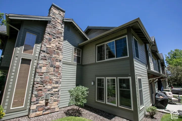 Multi-story exterior featuring lap siding, shake shingle accents, a full-height stone chimney, and multi-pane windows
