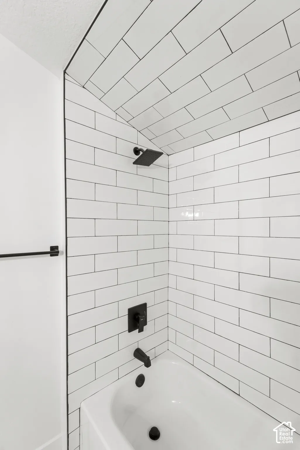 Shower area featuring white subway tile wall and ceiling surround, matte black rainfall showerhead, matte black diverter handle, matte black tub spout, and integrated towel bar