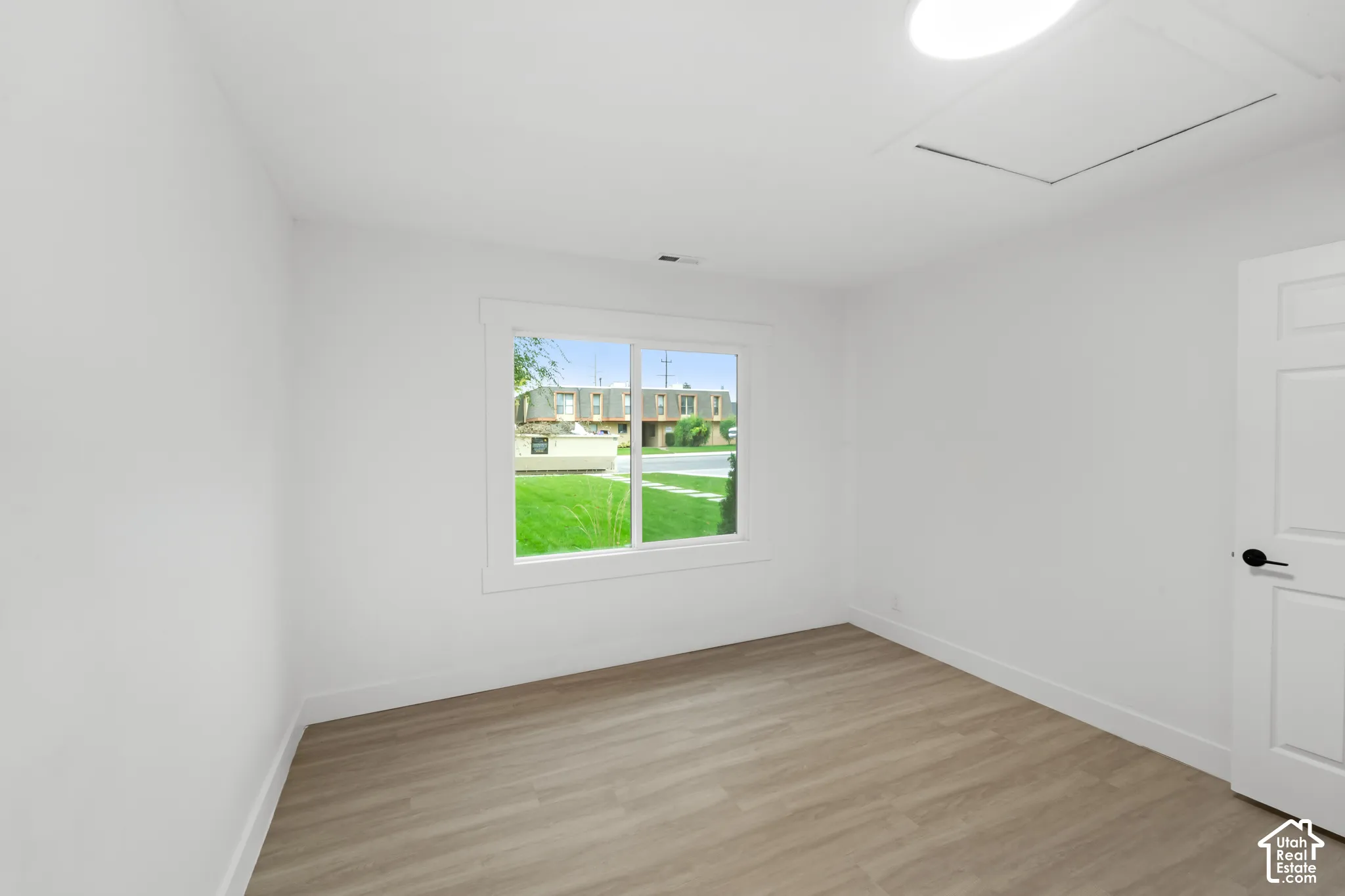Neutral-toned interior room featuring wood-finish flooring, a sliding window with clean white casing, a solid-panel door with matte black hardware, and an integrated ceiling light fixture