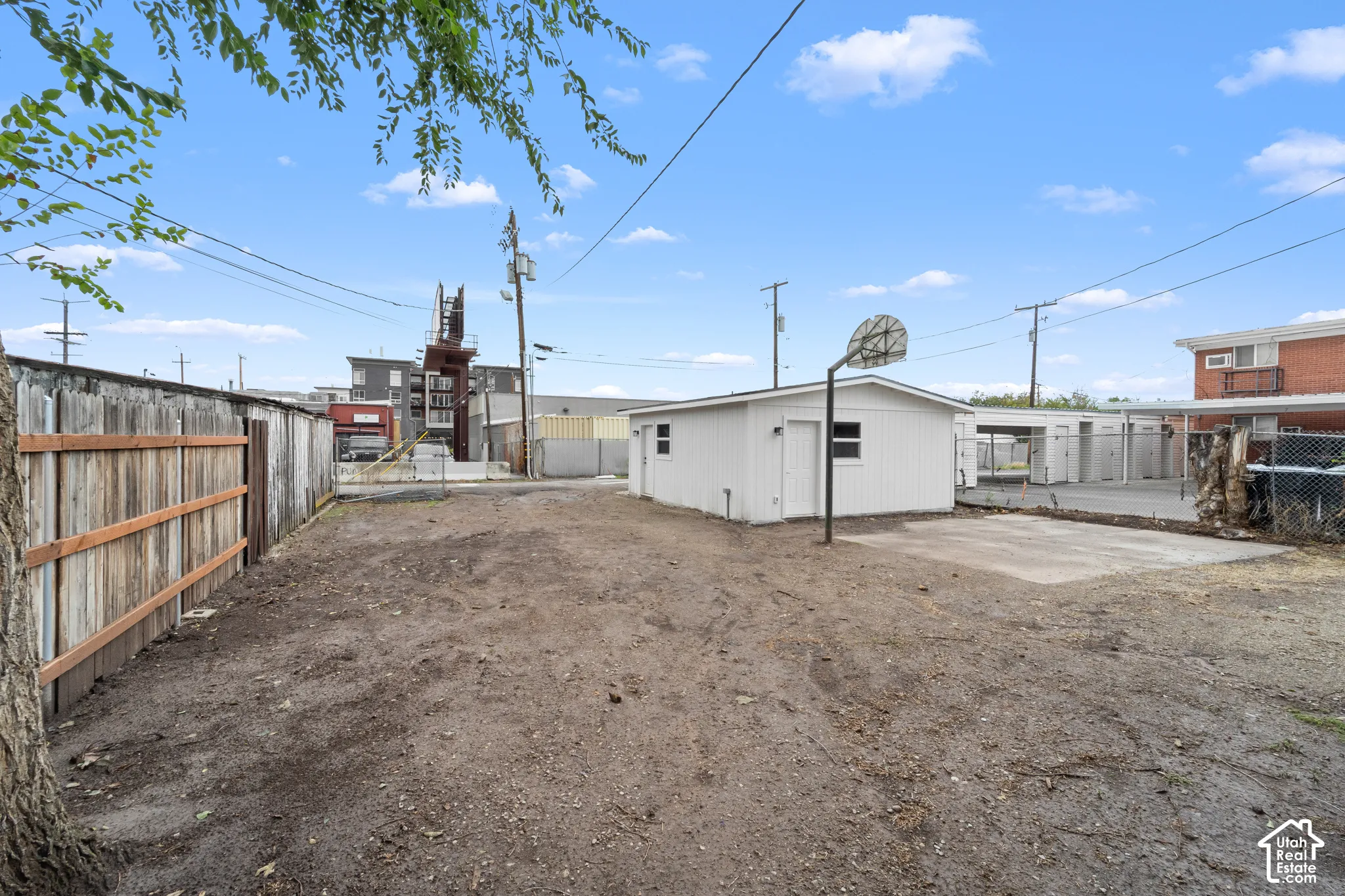 Exterior lot featuring a detached outbuilding, concrete pad, basketball hoop, and perimeter wood fencing