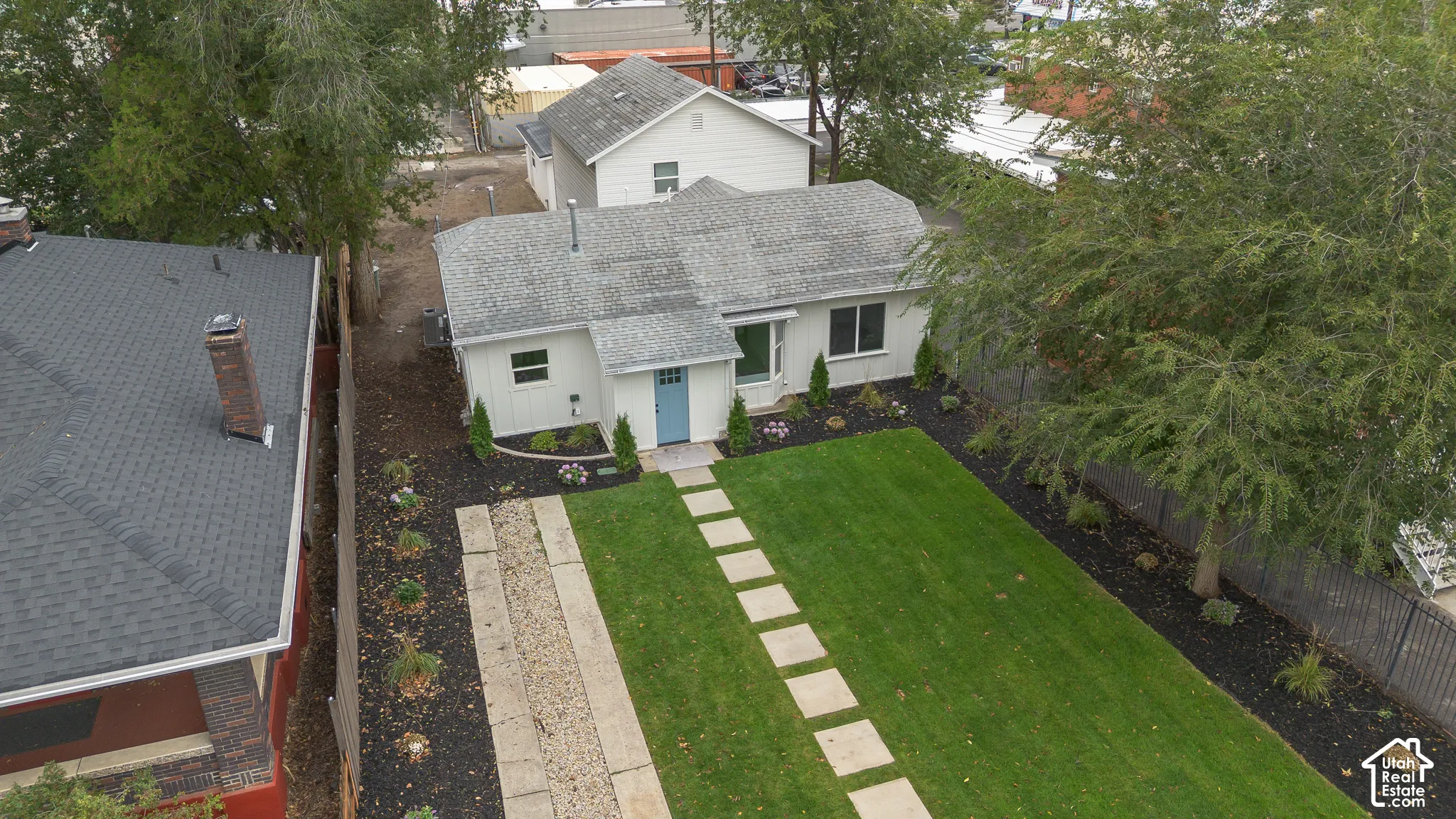 Single-story exterior featuring a light-toned facade, manicured lawn, stone paver walkway, and mature trees