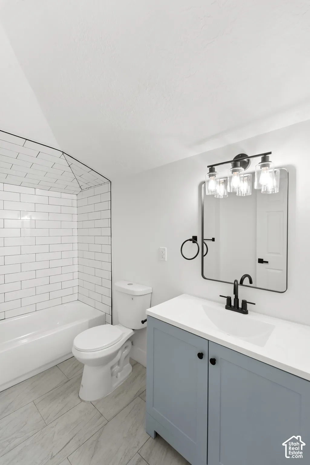 Bathroom featuring a vanity with a white countertop and matte black fixtures, rectangular framed mirror, tub surround with white subway tile, and wood-finish tile flooring