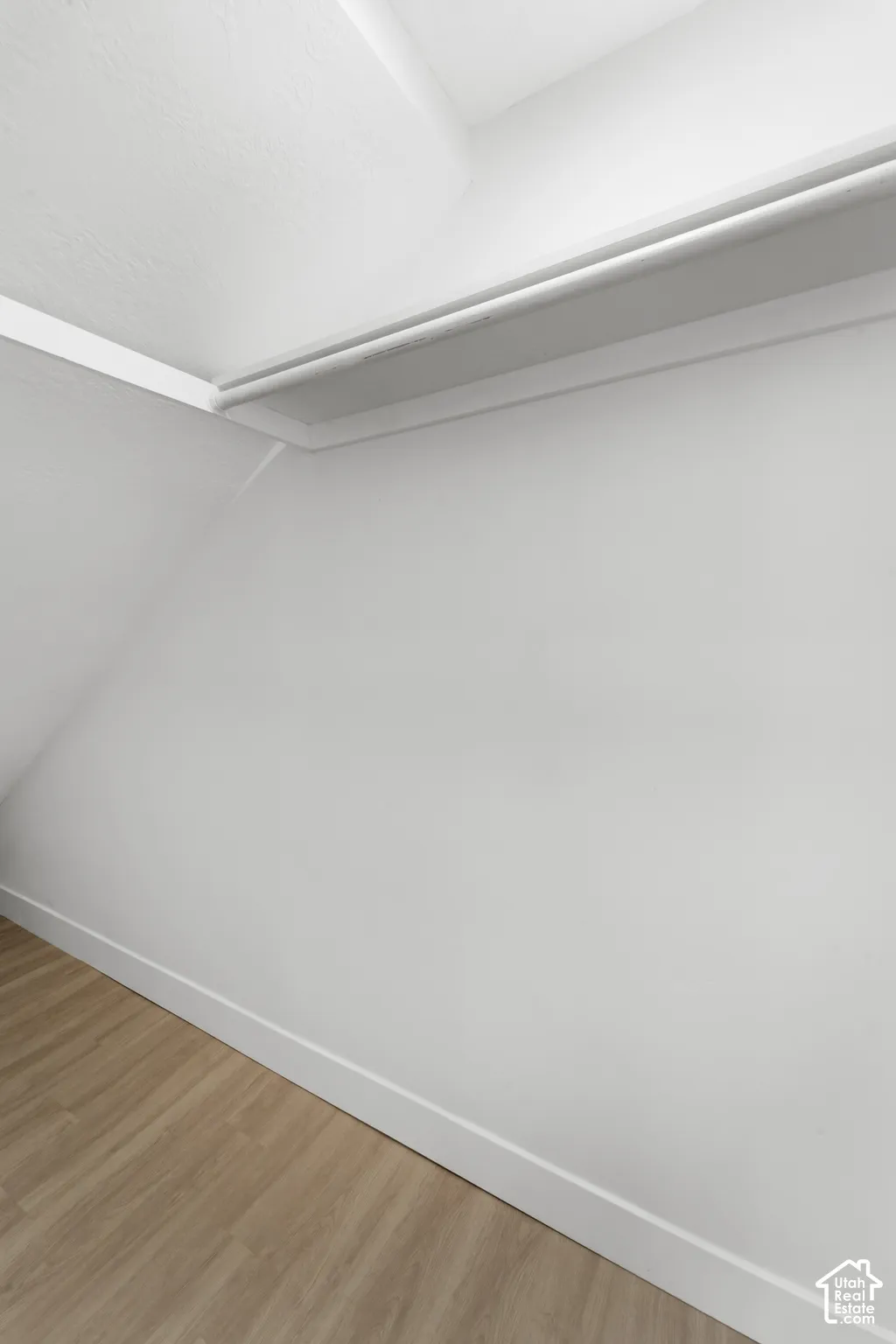 Interior storage area featuring a white built-in shelving unit, angled wall architecture, and wood-finish flooring