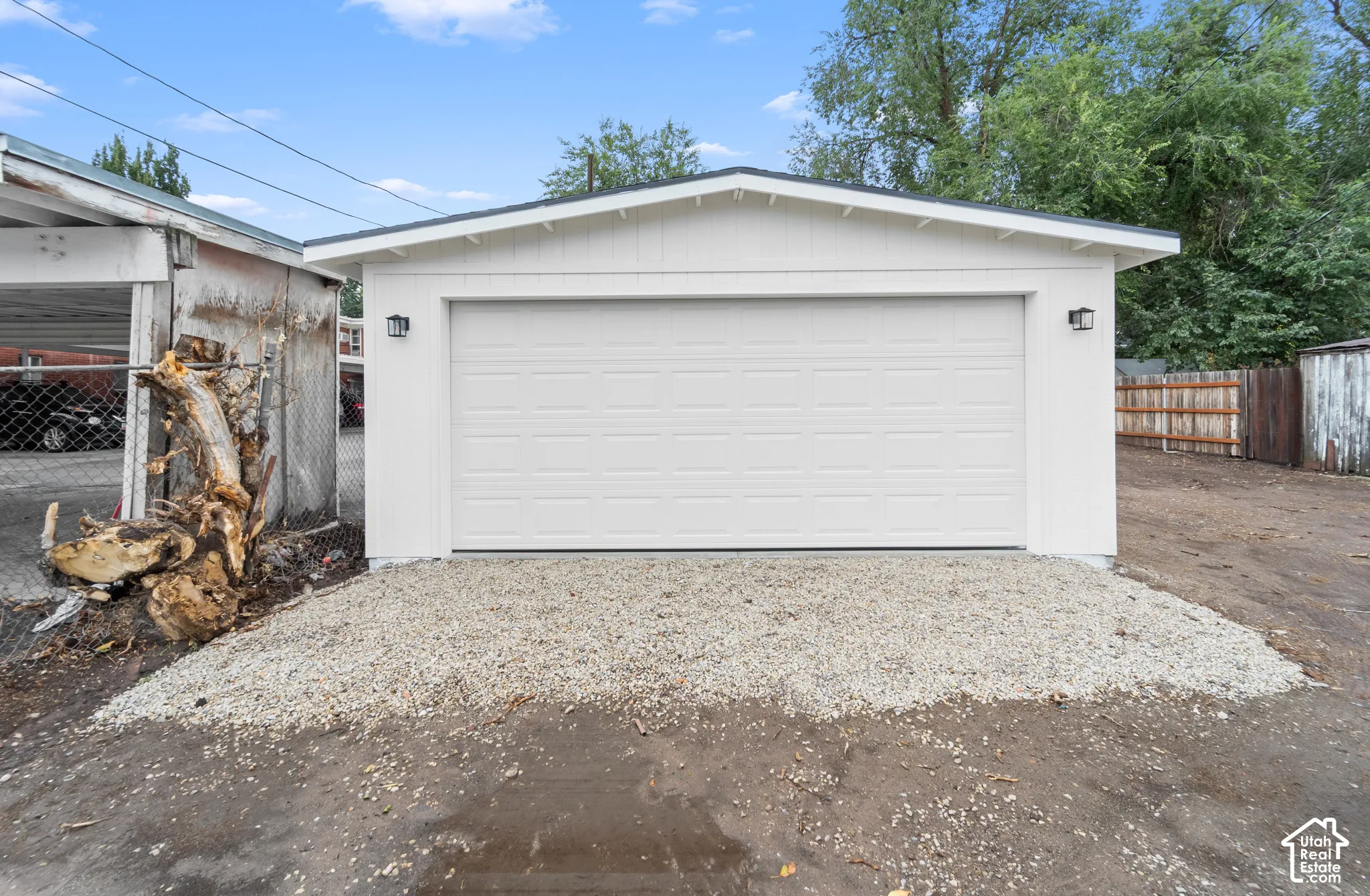Detached garage featuring white siding, a sectional door, and exterior wall-mounted lighting