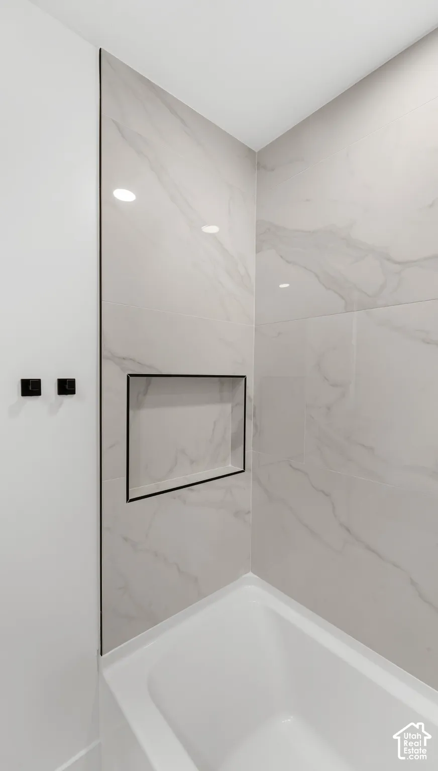 Shower surround featuring large-format tile with veining, integrated wall niche with matte black trim, and matching matte black wall-mounted hardware