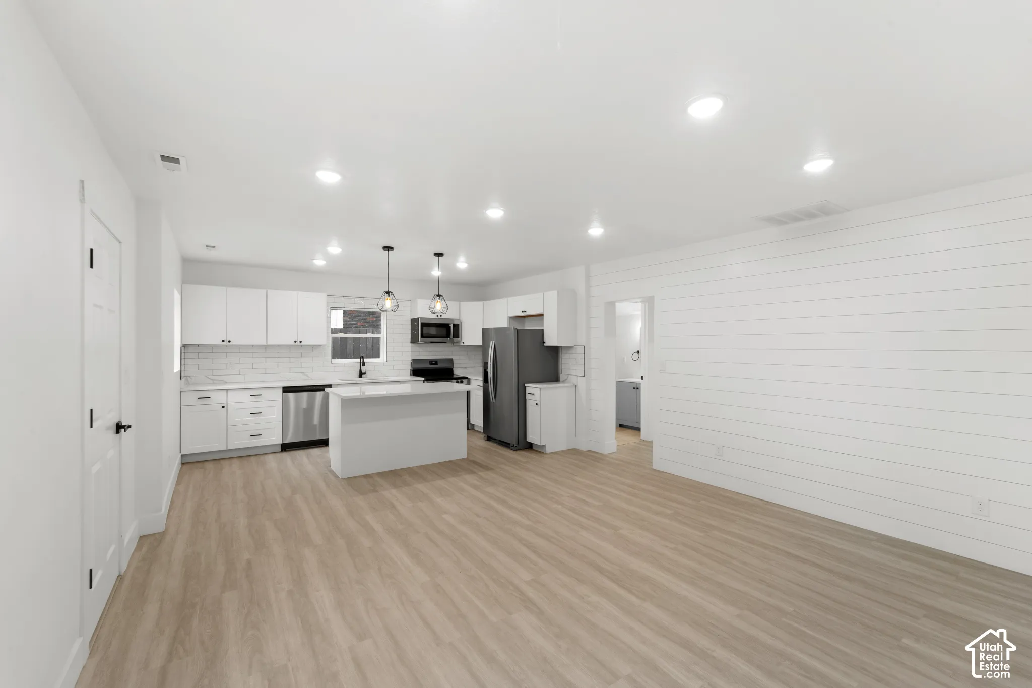 Open concept kitchen featuring white cabinetry, wood-finish flooring, a central island, stainless steel appliances, and horizontal shiplap wall detailing
