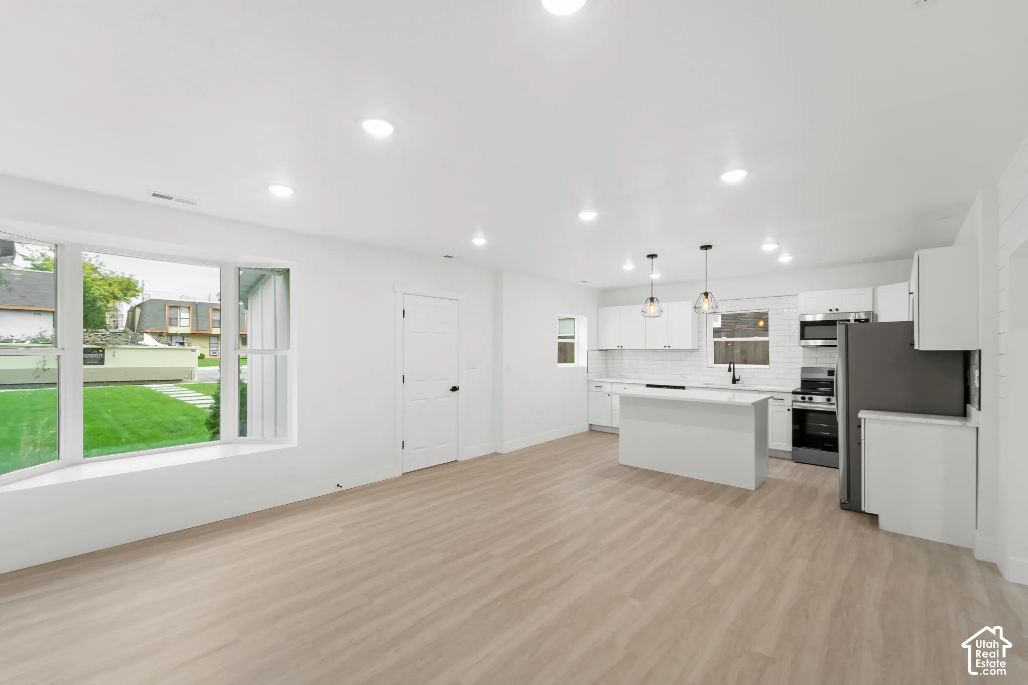 Open-concept interior featuring light wood-finish flooring, a center island with a stone countertop, recessed lighting, white cabinetry, and a large bay window