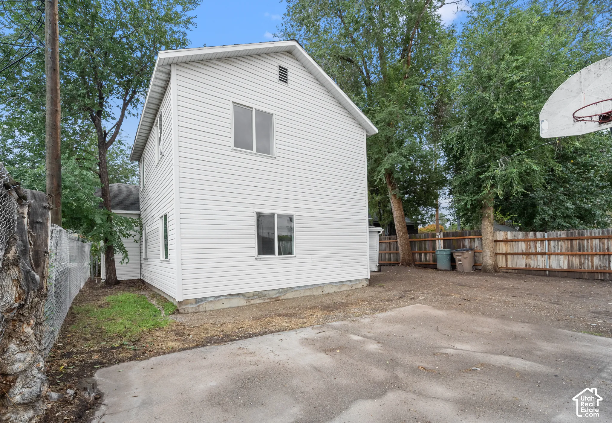 Two-story structure featuring white horizontal siding, a concrete parking pad, and perimeter fencing