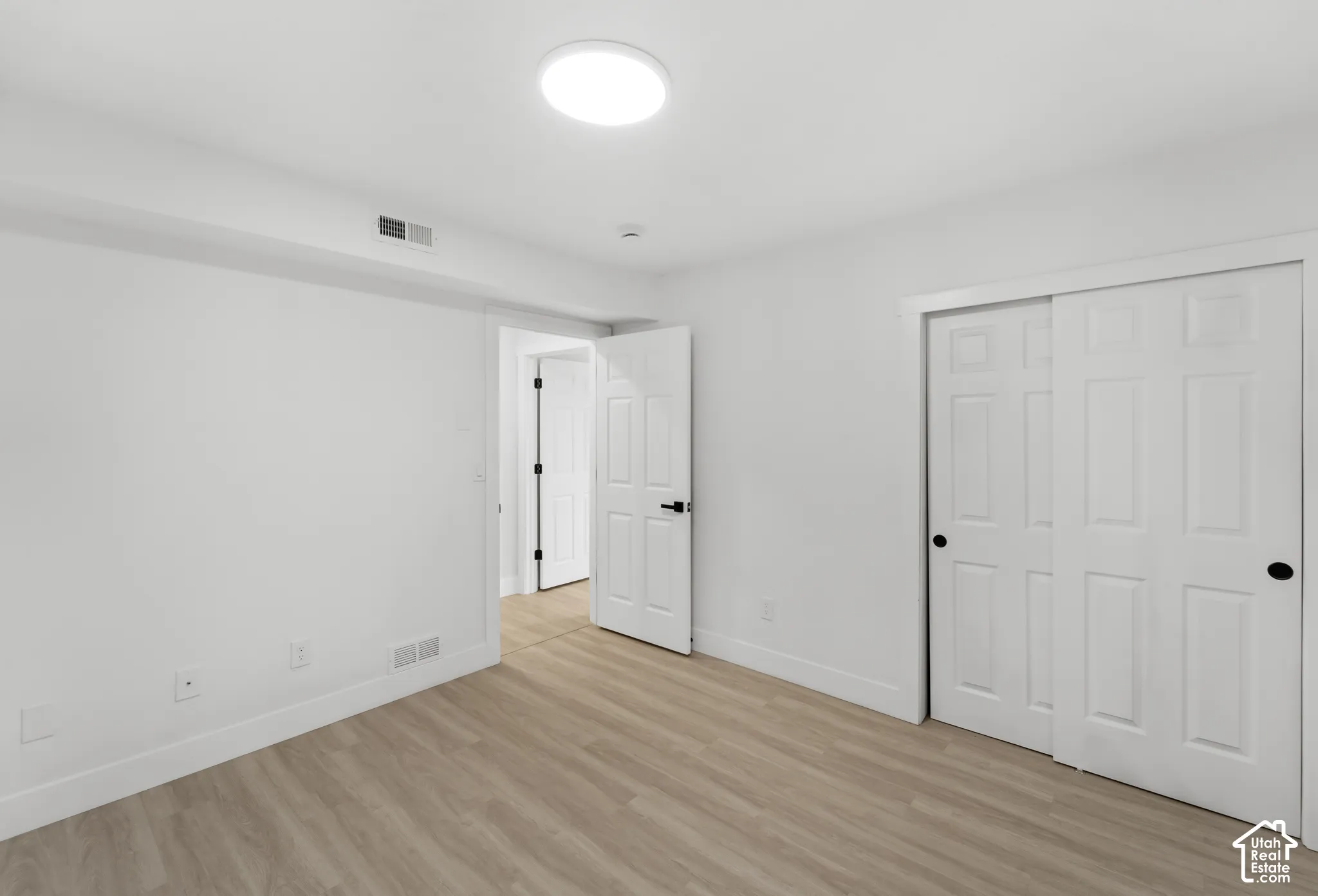 Neutral-toned room featuring wood-finish flooring, white six-panel doors with matte black hardware, dual-panel sliding closet, and a flush-mount circular ceiling light