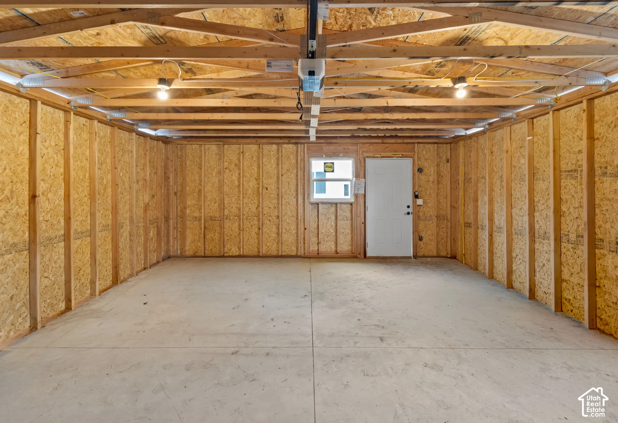 Unfinished garage interior featuring exposed wood framing, oriented strand board (OSB) wall panels, a concrete floor, an integrated door, and a single window