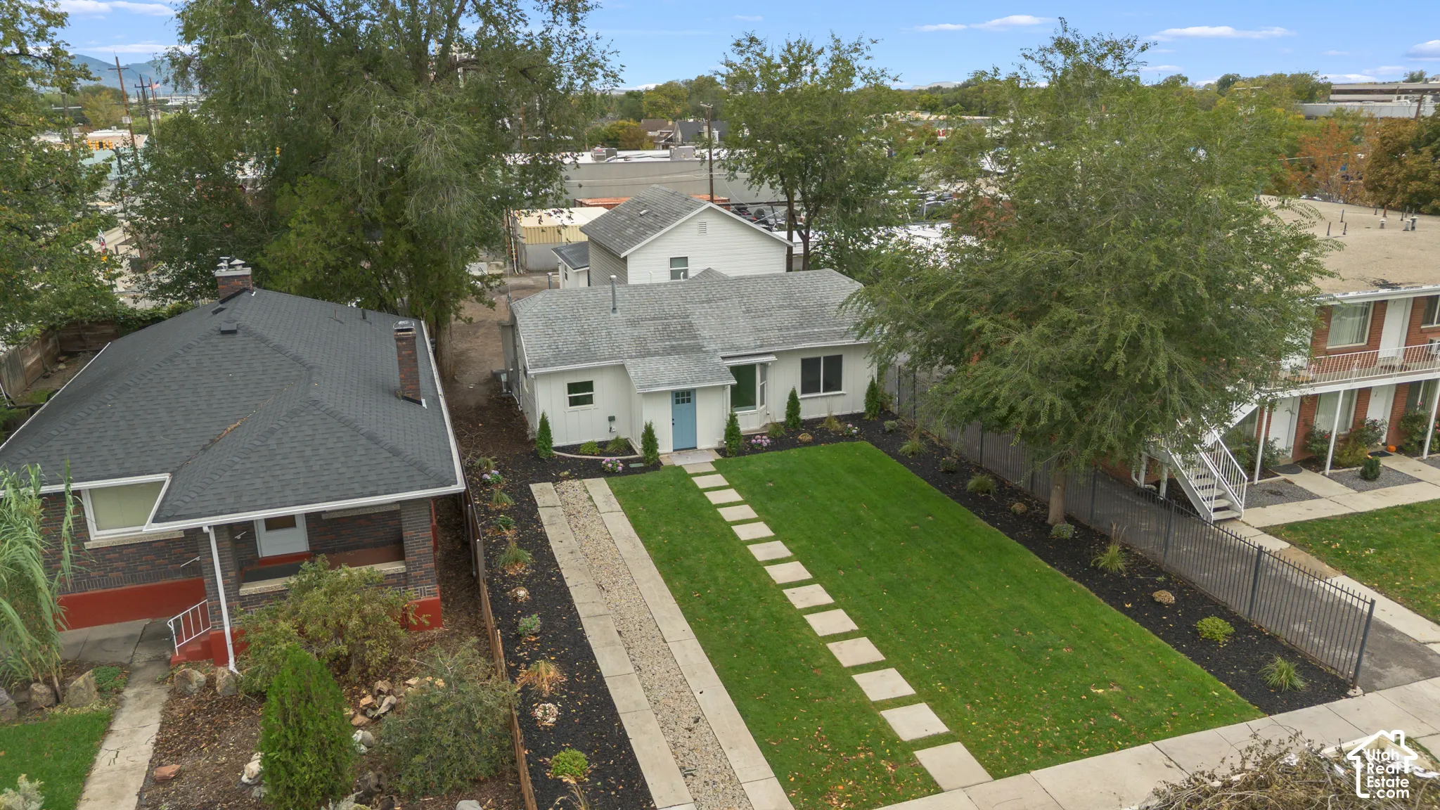 Exterior featuring white siding, a concrete paver walkway, manicured lawn, dark landscape mulch, and mature trees