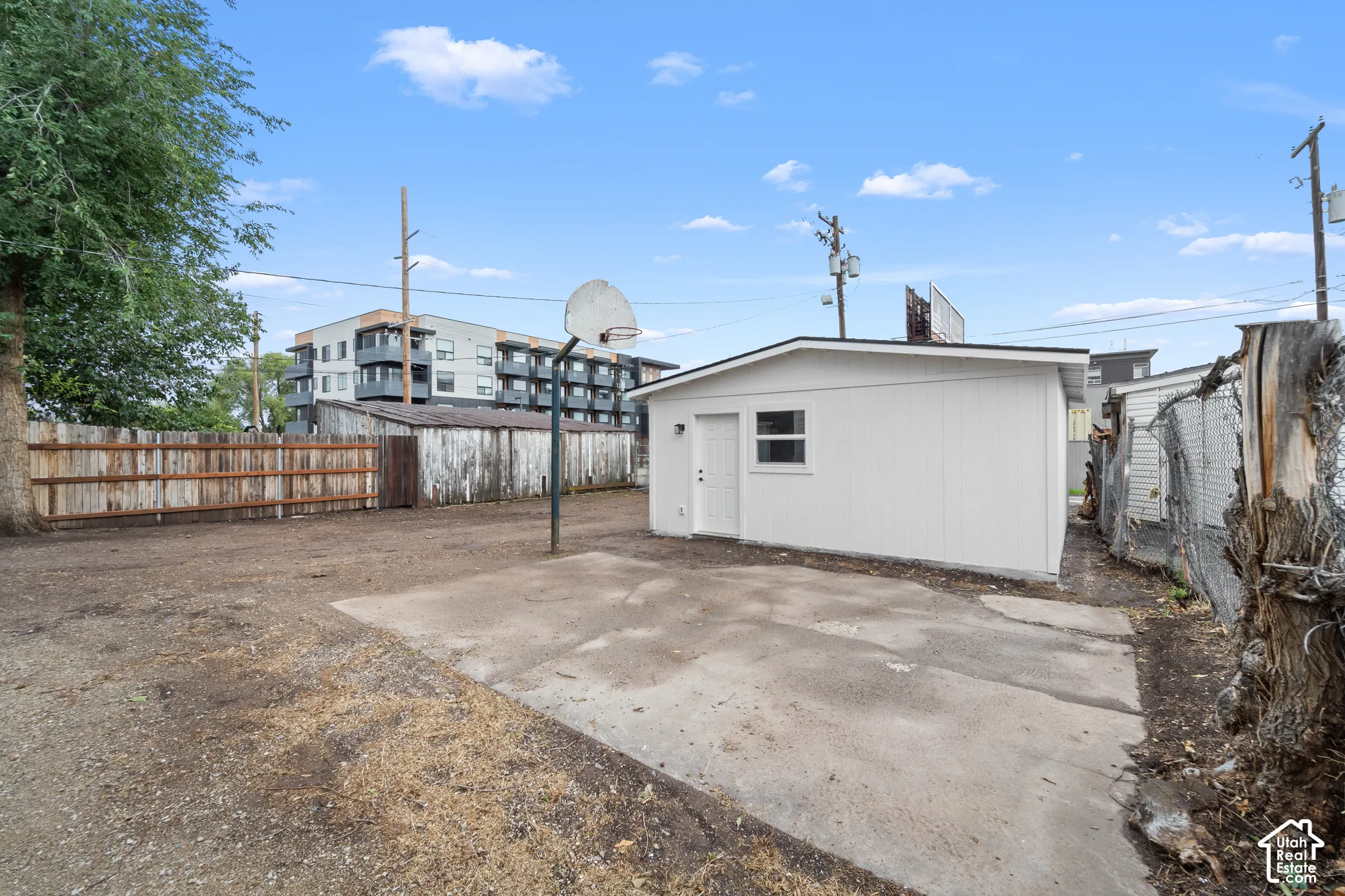 Detached exterior structure featuring white siding, concrete pad, and a basketball hoop within a fenced lot