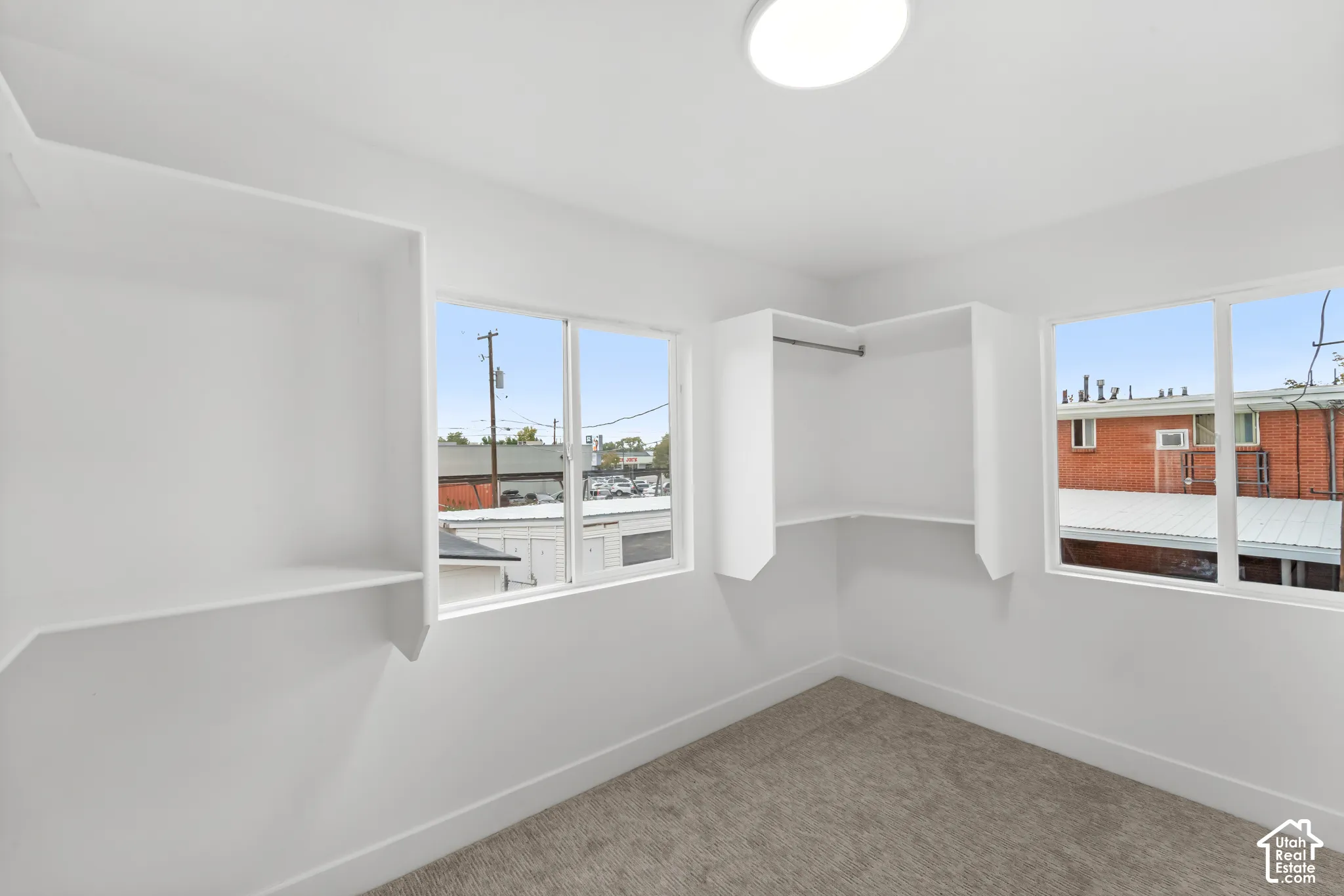 Room with neutral-toned carpeting, two dual-pane sliding windows, and built-in white shelving and hanging rods