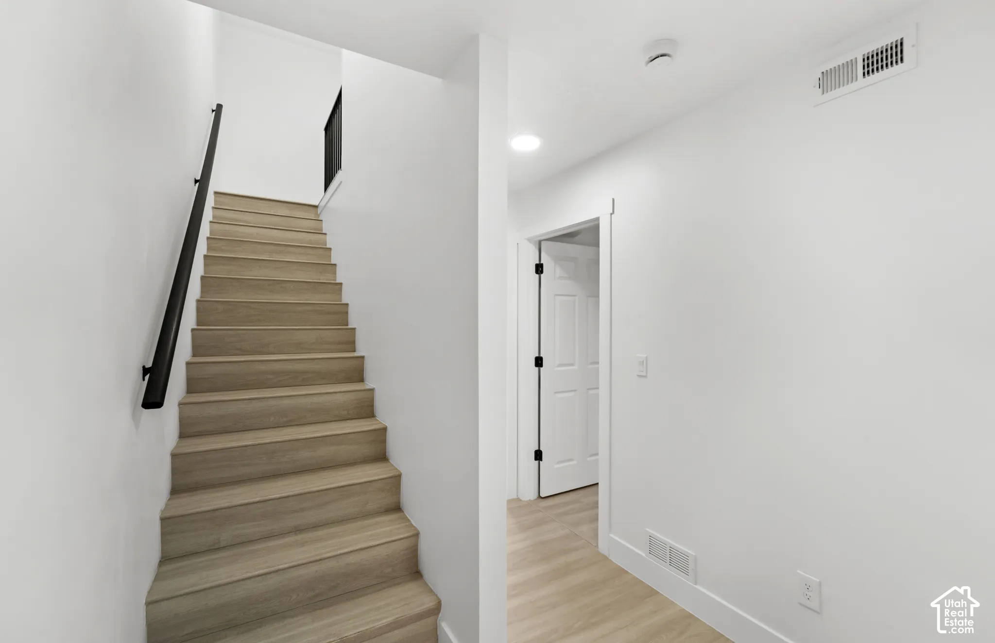 Staircase featuring wood-finish treads and a minimalist matte black handrail, complemented by wood-finish flooring and a white paneled door