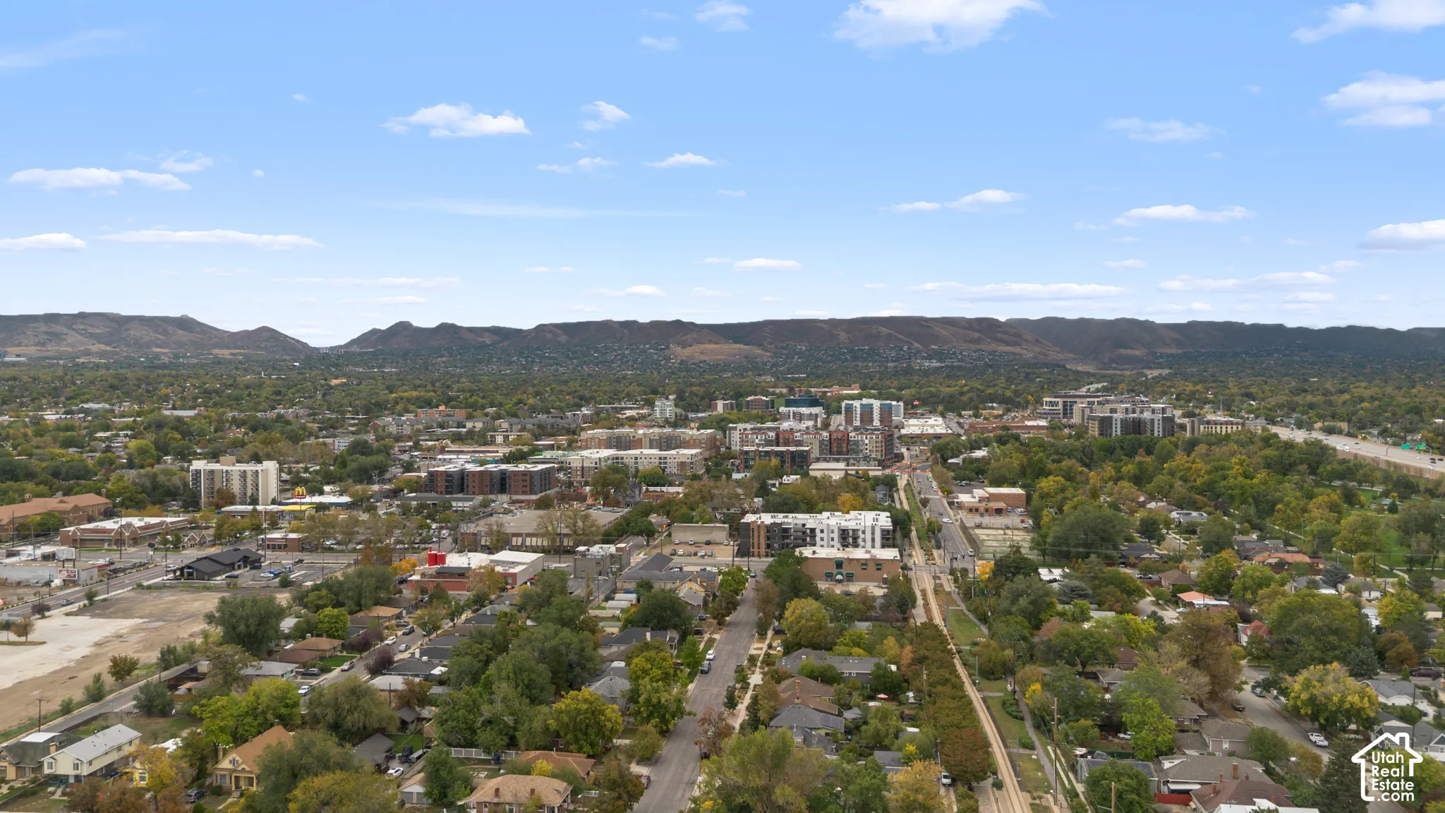 Aerial perspective of the metropolitan landscape featuring dense mature tree coverage, expansive mountain terrain, and regional infrastructure