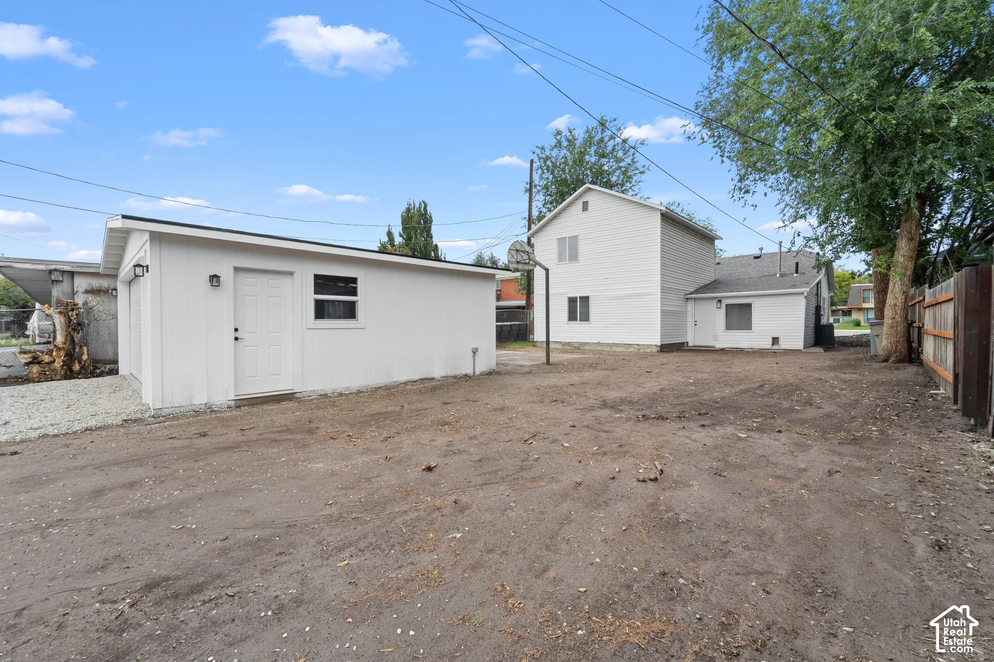 Detached garage featuring white siding, a single-car garage door, and a dedicated entry door, situated on a lot with an expansive cleared area and perimeter wood fencing