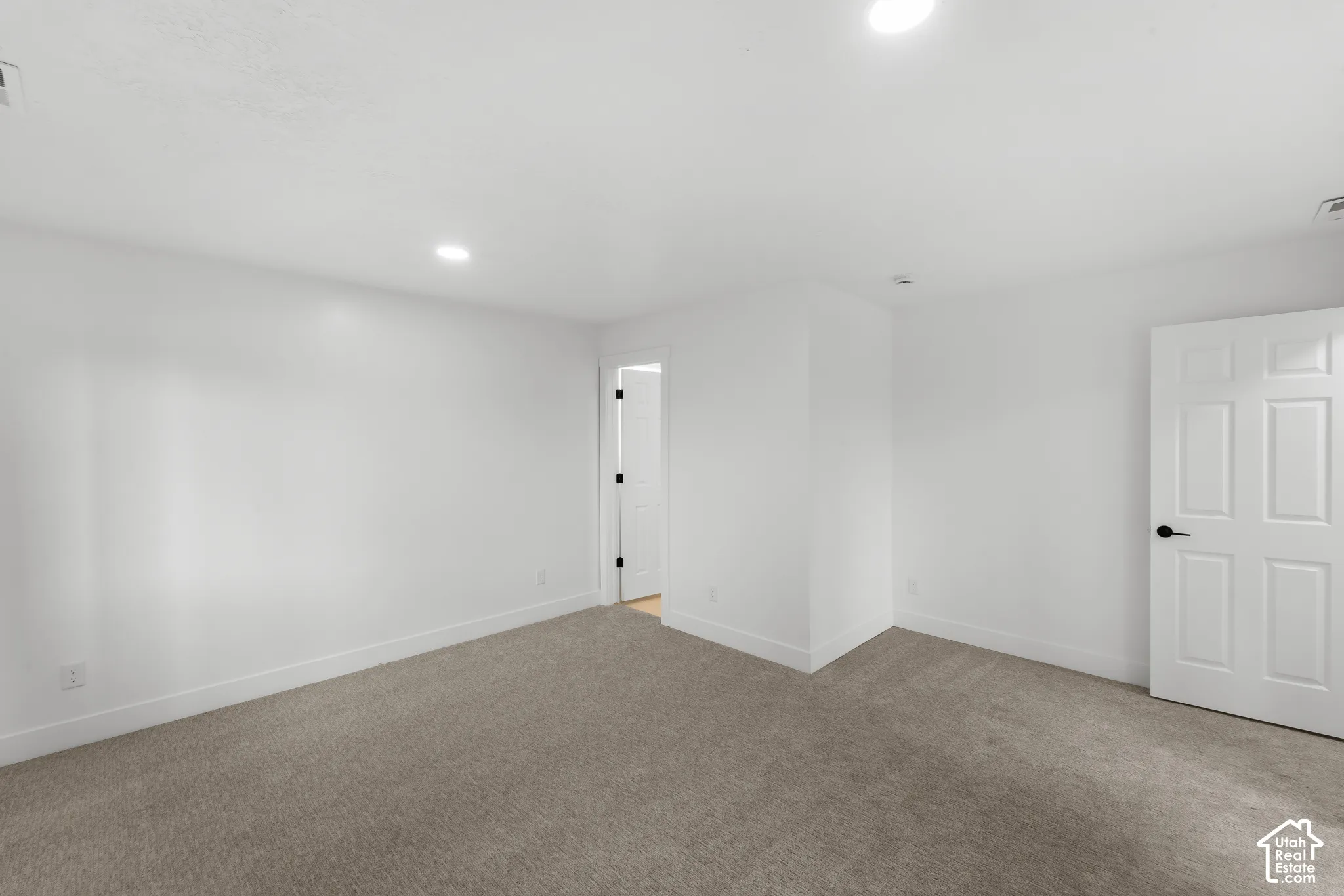 Neutral-toned carpeting, recessed ceiling lighting, and a six-panel door with matte black hardware