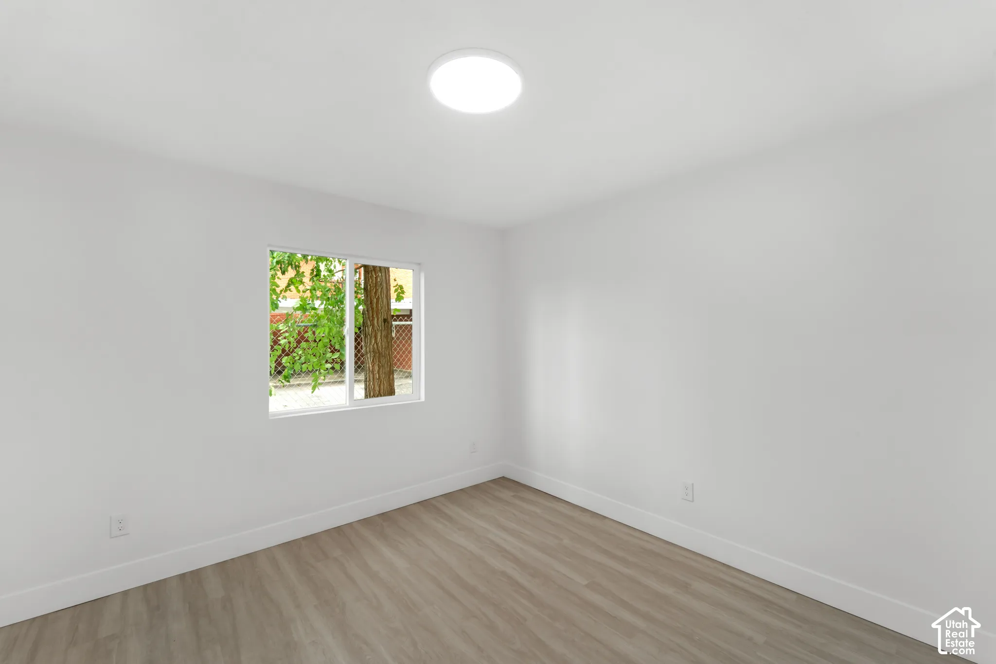 Neutral interior featuring wood-finish flooring, white walls, a sliding window, and a flush-mount ceiling light fixture