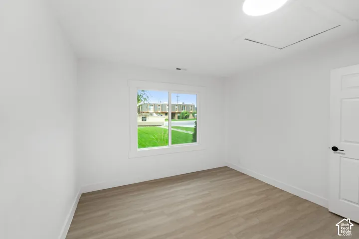 Neutral-toned interior room featuring wood-finish flooring, a sliding window with clean white casing, a solid-panel door with matte black hardware, and an integrated ceiling light fixture