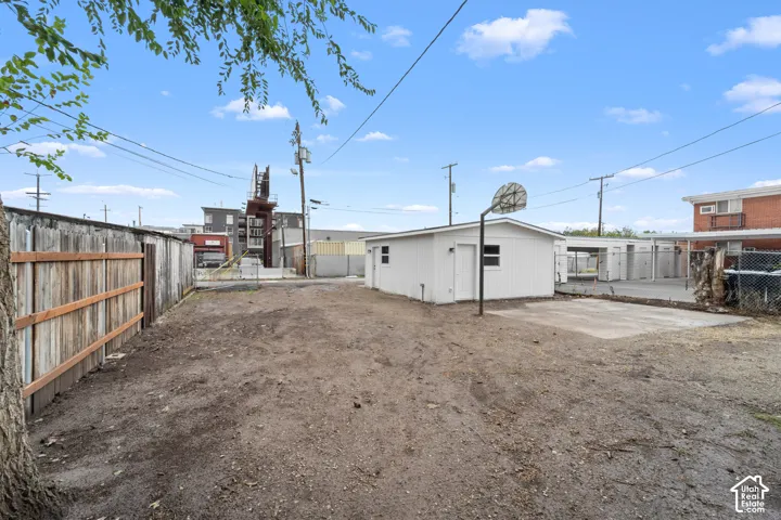 Exterior lot featuring a detached outbuilding, concrete pad, basketball hoop, and perimeter wood fencing