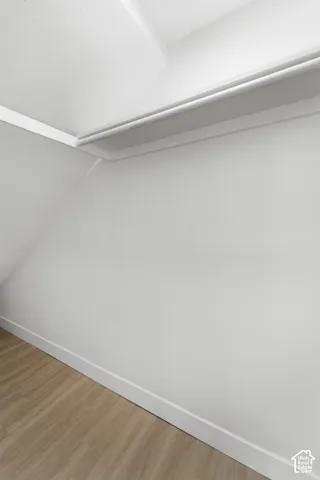 Interior storage area featuring a white built-in shelving unit, angled wall architecture, and wood-finish flooring