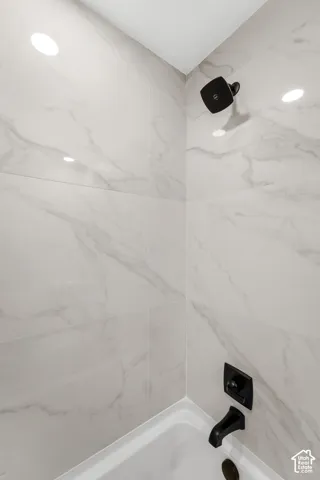 Shower surround featuring large-format light-toned stone-finish tile, matte black shower head, matching wall-mounted faucet, and built-in tub