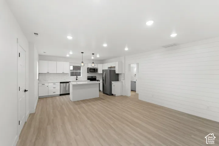 Open concept kitchen featuring white cabinetry, wood-finish flooring, a central island, stainless steel appliances, and horizontal shiplap wall detailing