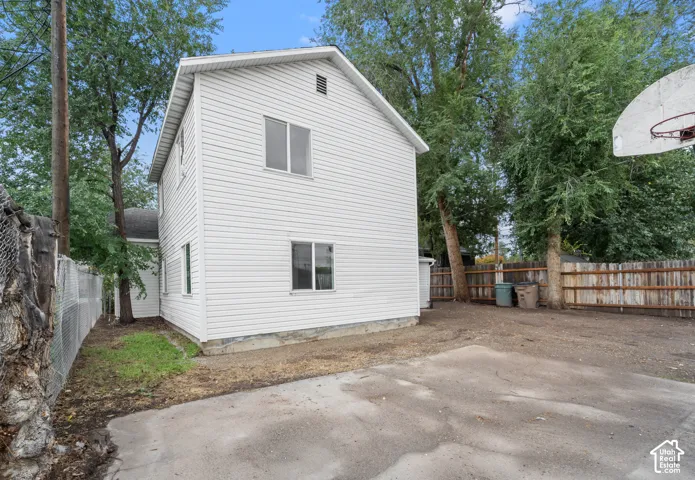Two-story structure featuring white horizontal siding, a concrete parking pad, and perimeter fencing