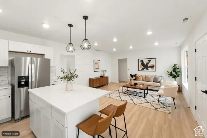 Kitchen featuring a central island with quartz countertop, white shaker-style cabinetry, stainless steel refrigerator, recessed lighting, and wood-finish flooring