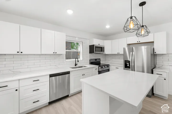 Kitchen featuring white shaker-style cabinetry, white countertops with grey veining, white subway tile backsplash, stainless steel appliances, and matte black geometric pendant lighting