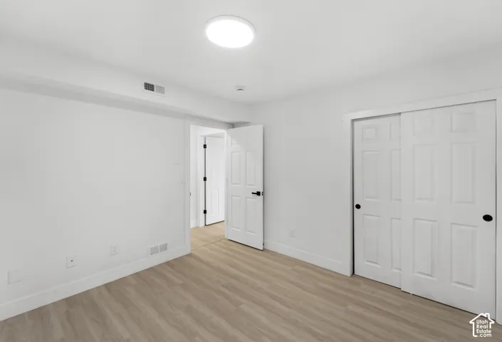 Neutral-toned room featuring wood-finish flooring, white six-panel doors with matte black hardware, dual-panel sliding closet, and a flush-mount circular ceiling light