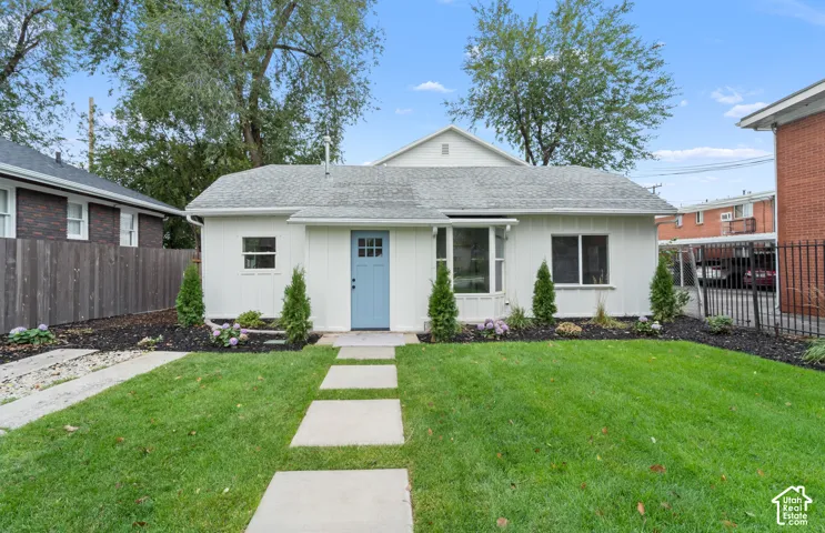 Single-story residence featuring white board-and-batten siding, a blue multi-pane entry door, a bay window, and a paved walkway leading to the home