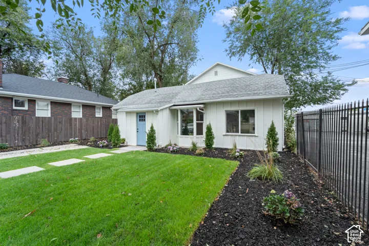 Vertical siding exterior featuring a multi-pane front door, bay window, manicured lawn, and structured landscape beds