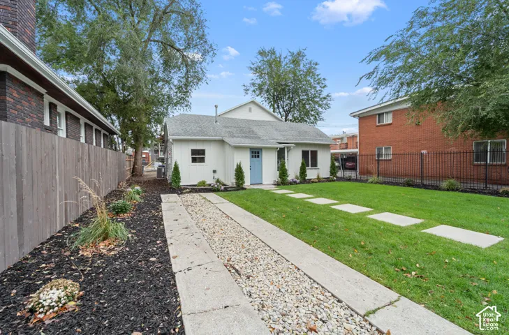Exterior backyard space featuring a manicured lawn, concrete paver pathway, decorative gravel strip, vertical wood-panel fencing, and mature trees
