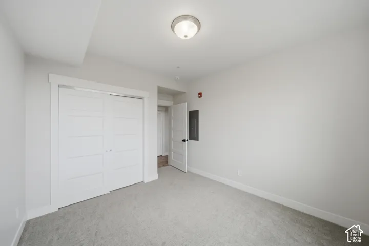 Spacious room featuring light gray carpet flooring, white walls, white trim, a flush mount ceiling light, and a two-panel sliding closet door