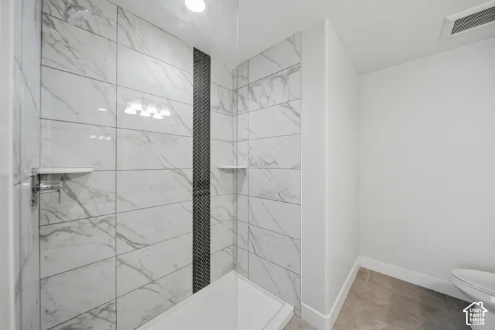 Walk-in shower featuring large format white marble-look tile, a chevron-patterned accent strip, chrome fixtures, and integrated shelving