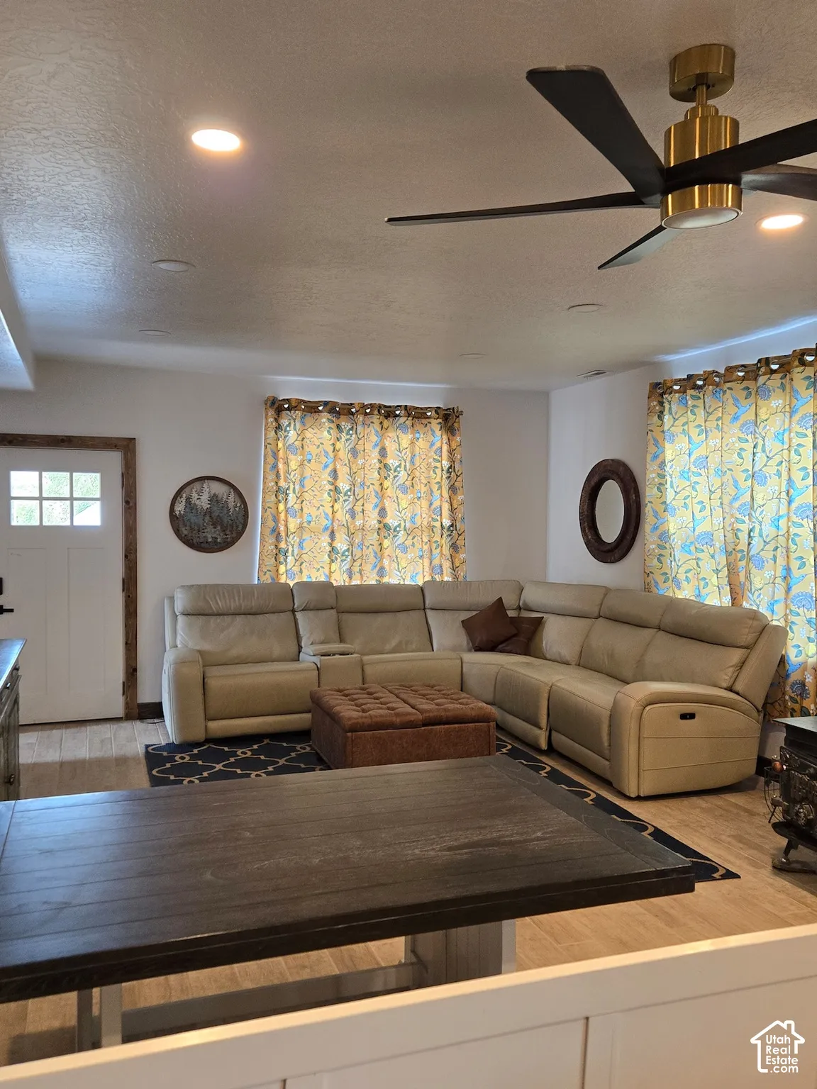 Modern living space featuring recessed lighting, a multi-blade ceiling fan with a metallic finish, wood-finish flooring, and a multi-panel door with wood-trim detailing