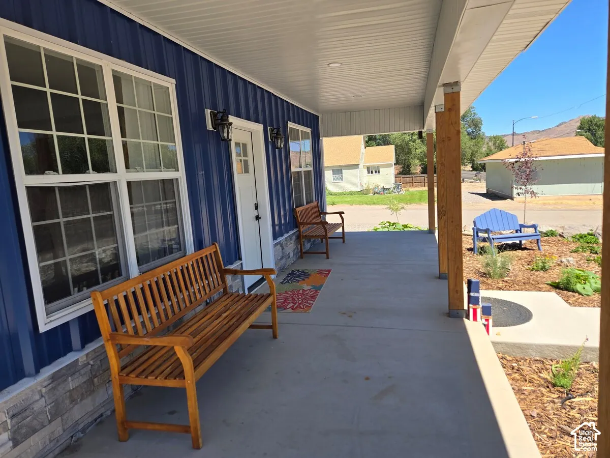 Covered front porch featuring vertical blue metal siding, stone veneer base, grid-pattern windows, and natural wood support columns