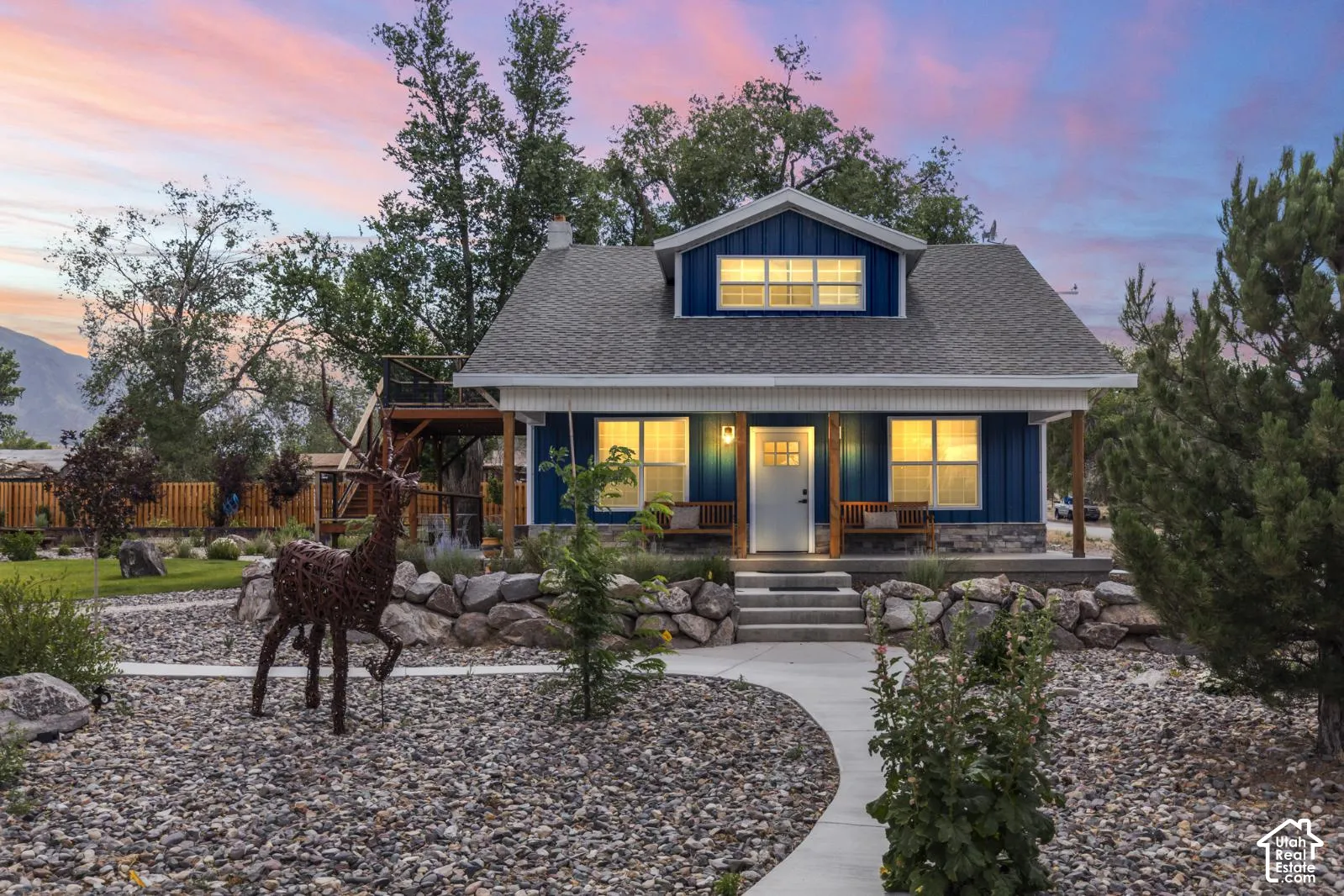 Blue vertical siding exterior featuring a stone masonry foundation, a covered front porch with timber support beams, and a concrete walkway