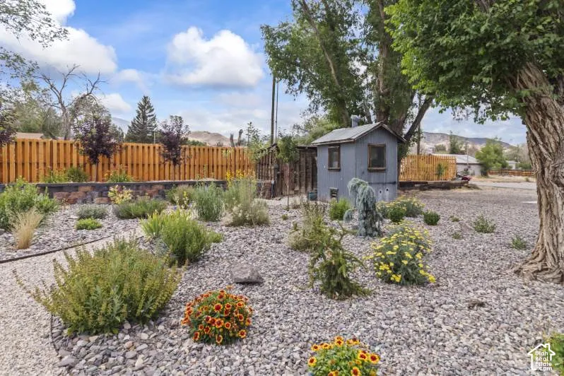 Xeriscaped grounds featuring decorative stone surfacing, native plantings, a vertical wood privacy fence, and a detached storage structure
