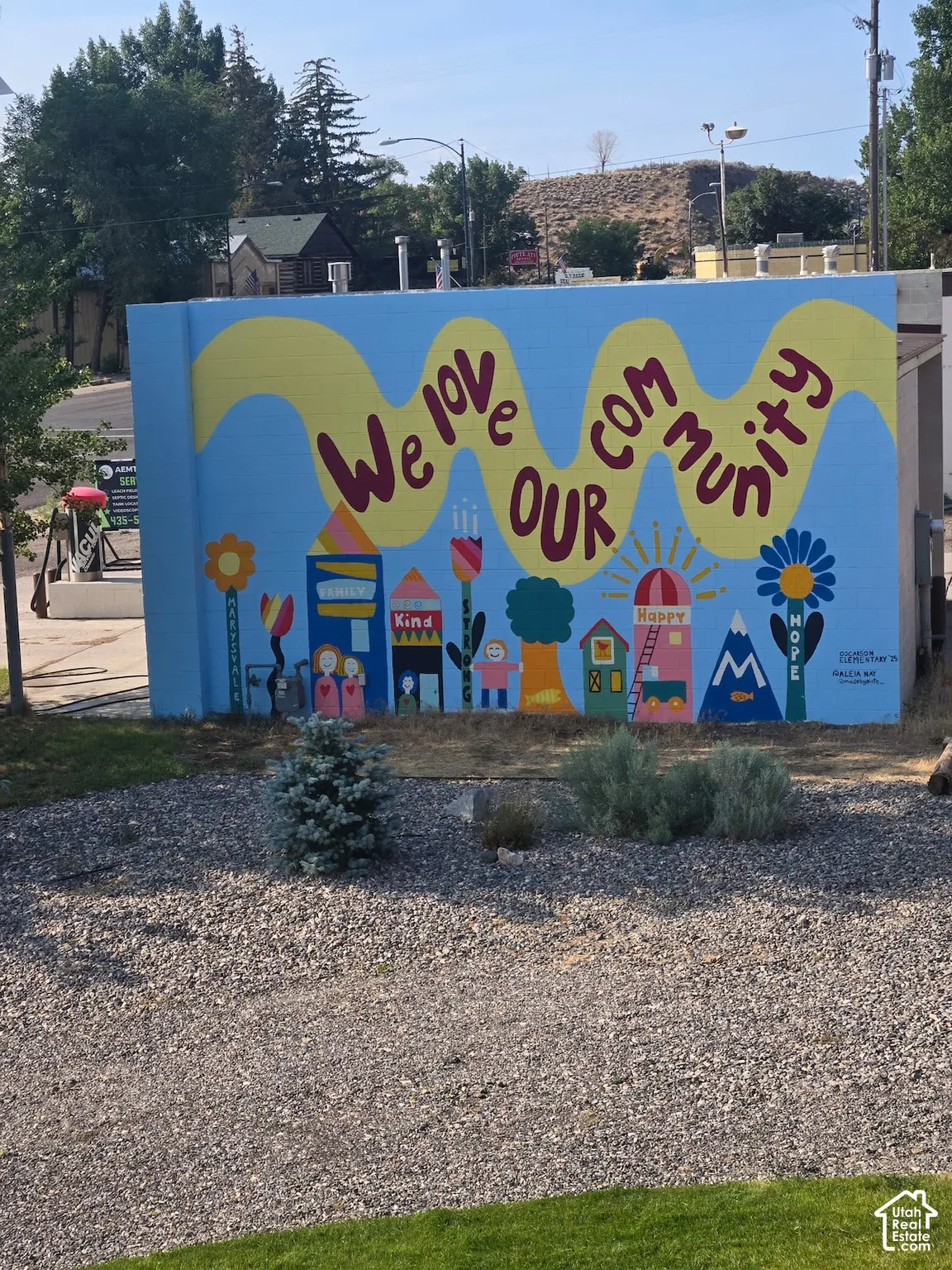 Exterior masonry wall featuring a painted mural, gravel landscaping, and mature shrubbery