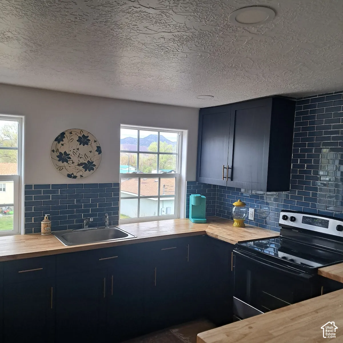 Kitchen featuring dark-finish cabinetry, butcher block countertops, blue subway tile backsplash, recessed ceiling lighting, and double-hung windows