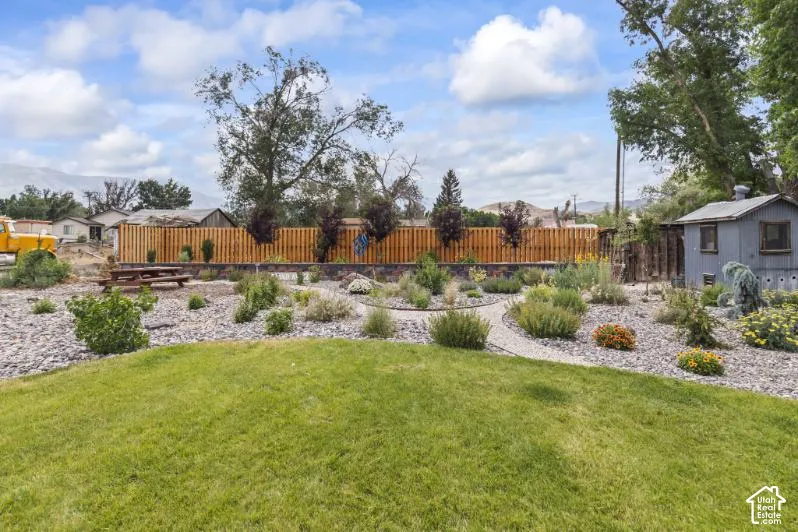 Expansive backyard featuring a natural grass lawn, xeriscaped garden beds with stone ground cover, a perimeter wood privacy fence, a stone retaining wall, and an exterior storage structure