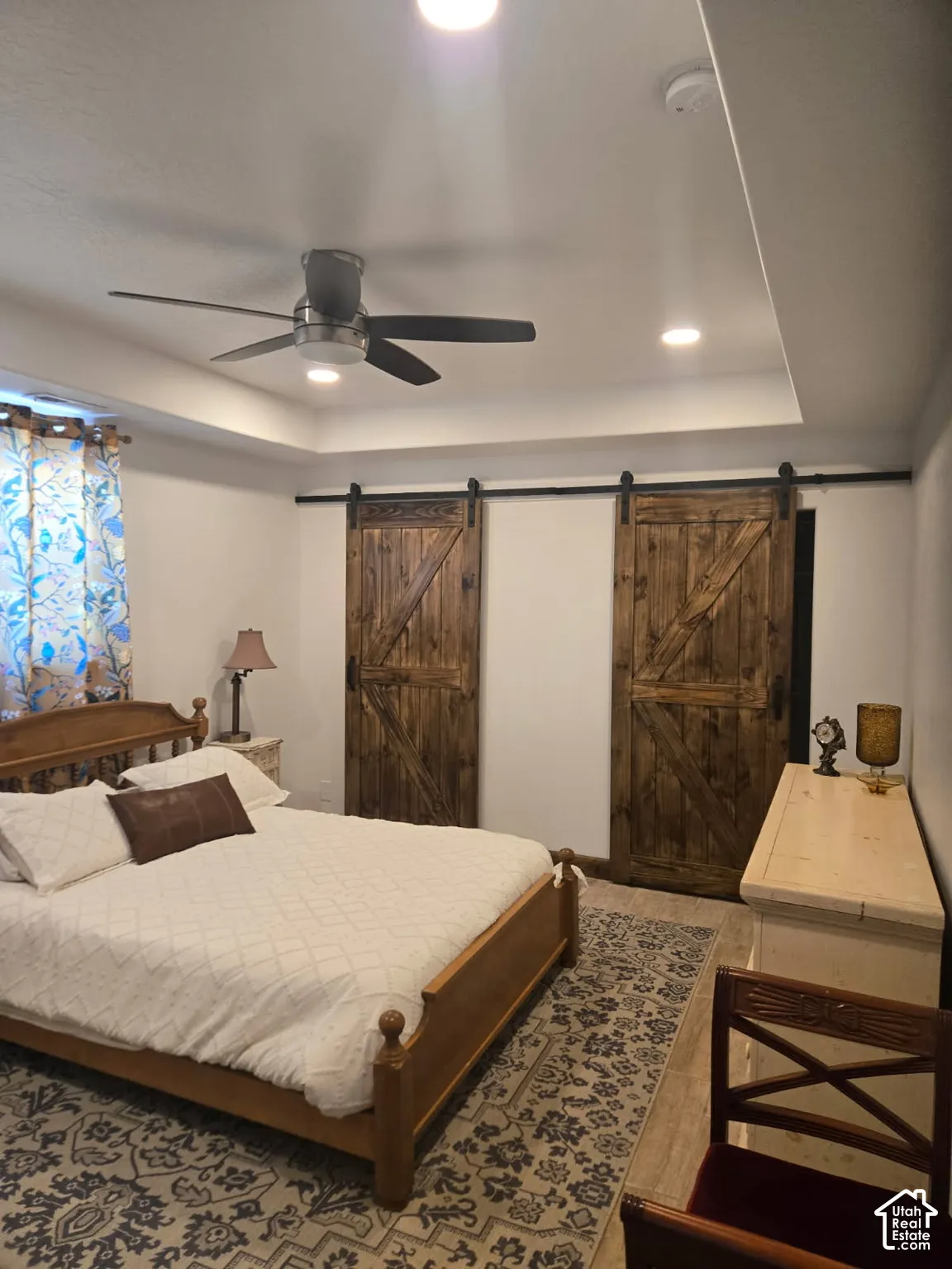 Tray ceiling with recessed lighting, dual sliding barn-style doors with black hardware, and wood-finish flooring