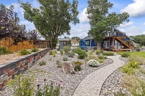 Landscaped backyard featuring tiered stone retaining walls, a meandering gravel path, mature trees, and an elevated wood deck