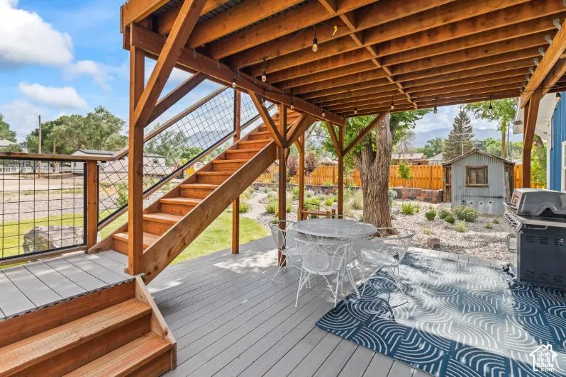 Covered lower-level patio featuring wood-framed structural beams, an integrated staircase with metal wire railing, and a composite deck surface