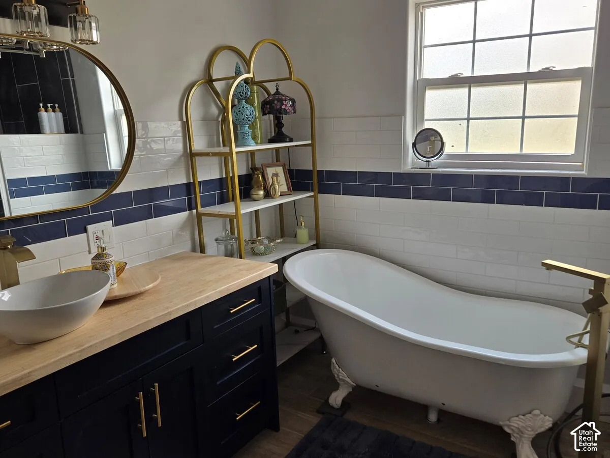 Bathroom featuring a white clawfoot tub, a wood-finish countertop vanity with a vessel sink, brass-finish hardware, and dual-tone subway tile backsplash