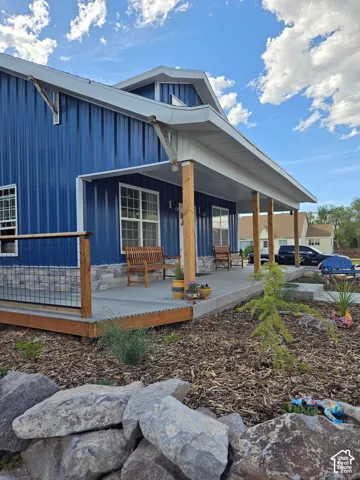 Exterior featuring blue vertical metal siding, covered porch with wood support posts, stone veneer skirting, and wire-mesh railing